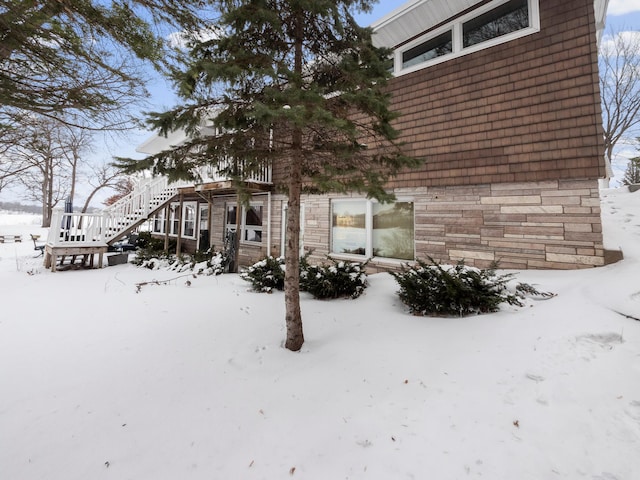 view of snowy exterior featuring stone siding and stairway