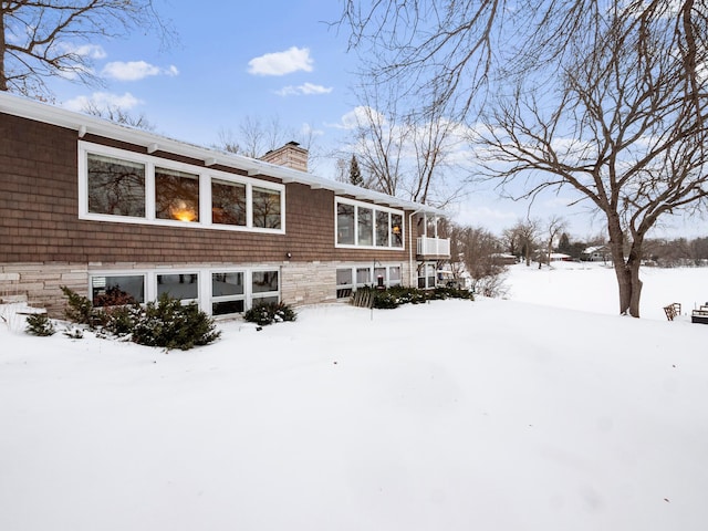 snow covered rear of property with a chimney