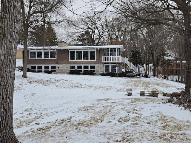 snow covered rear of property with a chimney and stairs