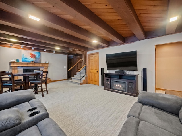 living room with beam ceiling, light colored carpet, stairway, a glass covered fireplace, and baseboards