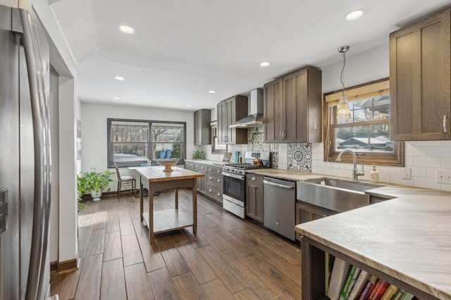 kitchen featuring pendant lighting, sink, dark hardwood / wood-style flooring, stainless steel appliances, and wall chimney exhaust hood