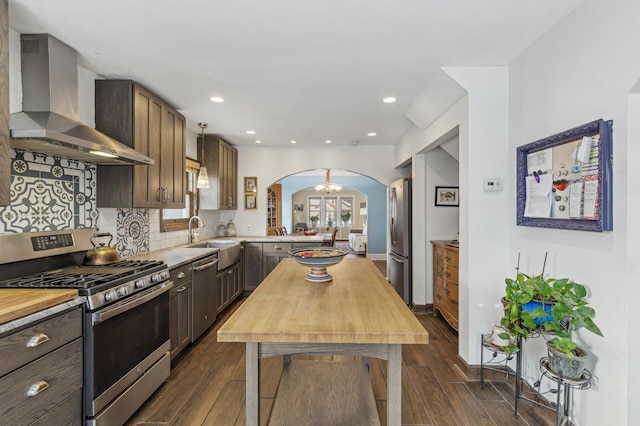 kitchen with tasteful backsplash, wall chimney range hood, sink, hanging light fixtures, and appliances with stainless steel finishes