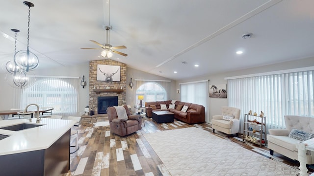 living room with sink, wood-type flooring, lofted ceiling, a fireplace, and ceiling fan with notable chandelier