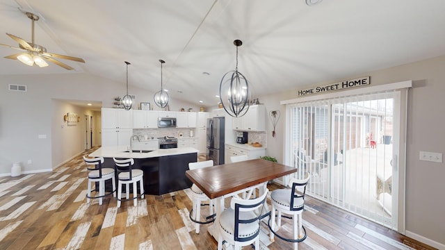 dining area with ceiling fan with notable chandelier, light hardwood / wood-style floors, vaulted ceiling, and sink