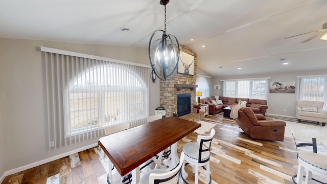 dining room with ceiling fan with notable chandelier, lofted ceiling, a fireplace, and light hardwood / wood-style flooring