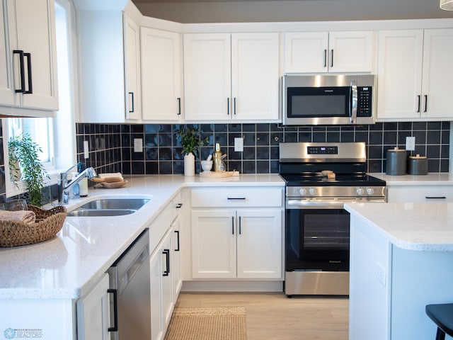 kitchen featuring sink, white cabinetry, light hardwood / wood-style floors, stainless steel appliances, and light stone countertops