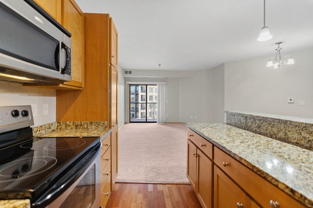 kitchen featuring stainless steel appliances, light stone countertops, hanging light fixtures, and light colored carpet