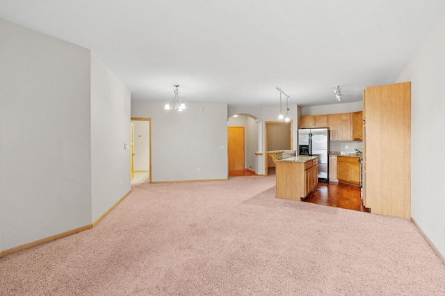 kitchen with stainless steel fridge, hanging light fixtures, a center island, light stone countertops, and dark carpet