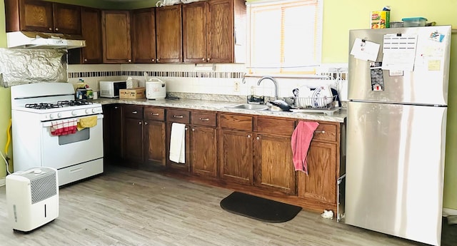 kitchen with exhaust hood, sink, light hardwood / wood-style flooring, white gas range, and stainless steel refrigerator