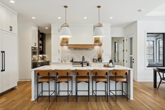 kitchen featuring white cabinetry, backsplash, an island with sink, pendant lighting, and a kitchen bar