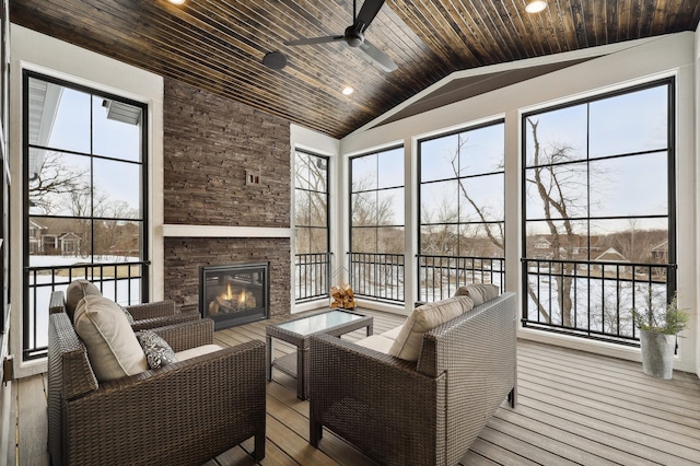 sunroom / solarium with ceiling fan, a stone fireplace, a water view, and vaulted ceiling