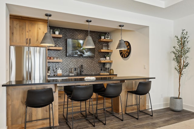 bar with decorative backsplash, sink, hanging light fixtures, and stainless steel refrigerator