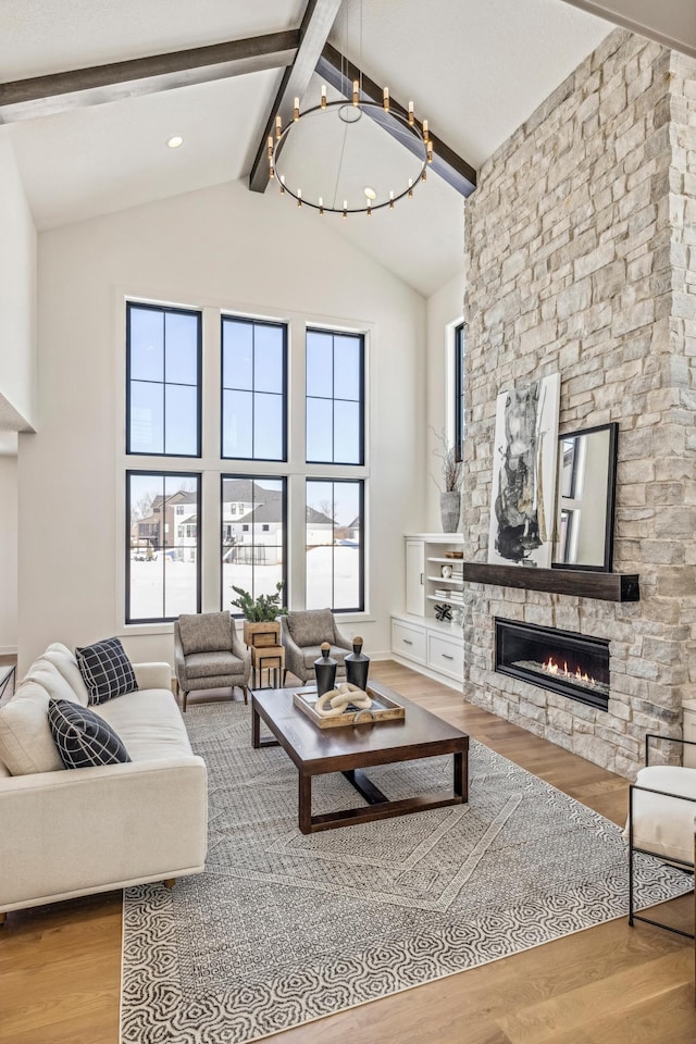 living room featuring light wood-type flooring, beam ceiling, high vaulted ceiling, a notable chandelier, and a stone fireplace