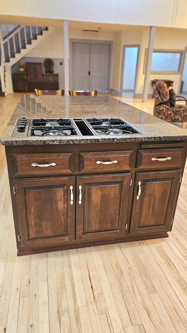 kitchen with dark brown cabinets, stone counters, light hardwood / wood-style floors, and gas cooktop