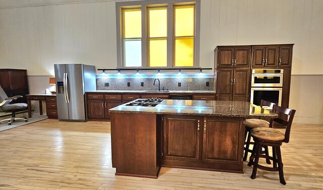 kitchen with a kitchen island, dark stone counters, a kitchen breakfast bar, stainless steel appliances, and dark brown cabinets