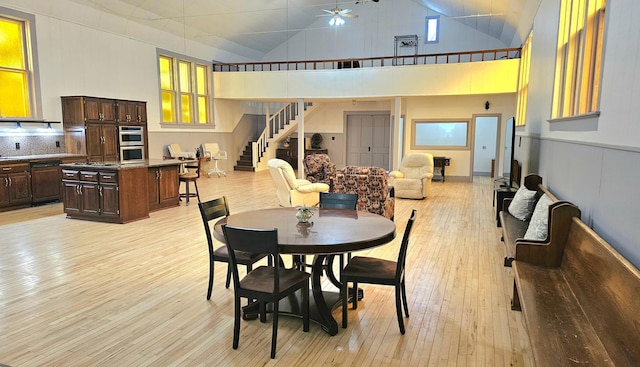 dining area with high vaulted ceiling, ceiling fan, and light wood-type flooring