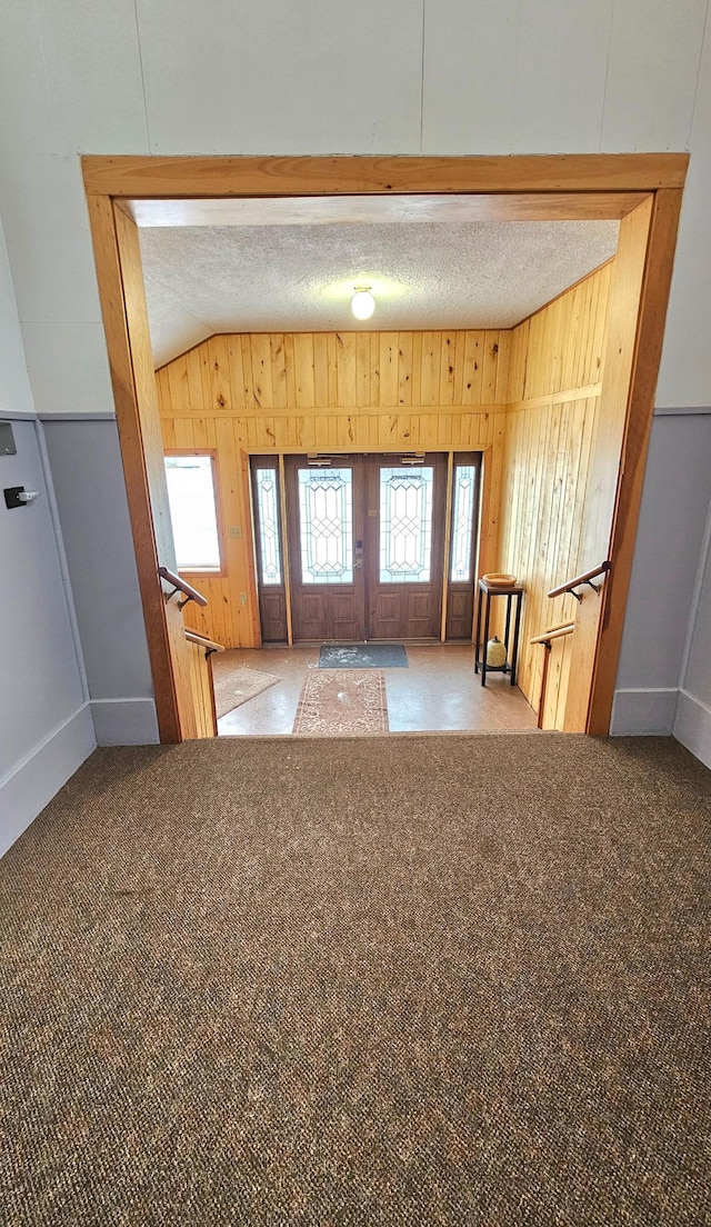 interior space with wood walls, a textured ceiling, light carpet, and lofted ceiling