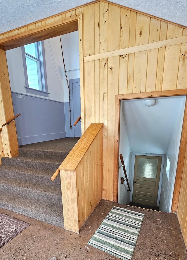 stairway with vaulted ceiling, a textured ceiling, and wood walls