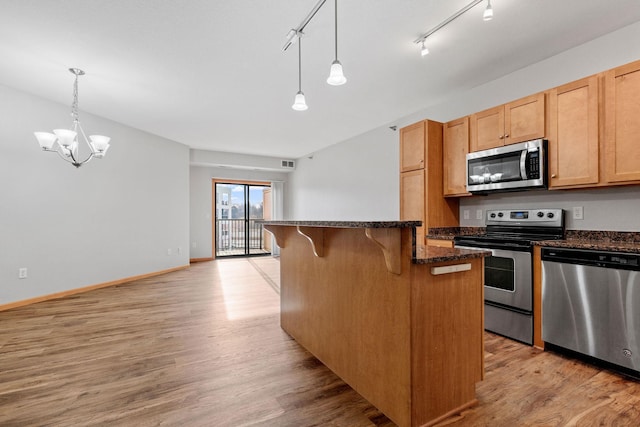 kitchen with a breakfast bar area, dark stone countertops, stainless steel appliances, decorative light fixtures, and light wood-type flooring