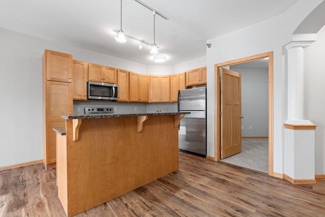 kitchen with ornate columns, a kitchen island, appliances with stainless steel finishes, a breakfast bar, and hardwood / wood-style flooring