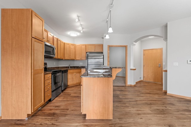 kitchen featuring hanging light fixtures, stainless steel appliances, a center island, wood-type flooring, and dark stone counters