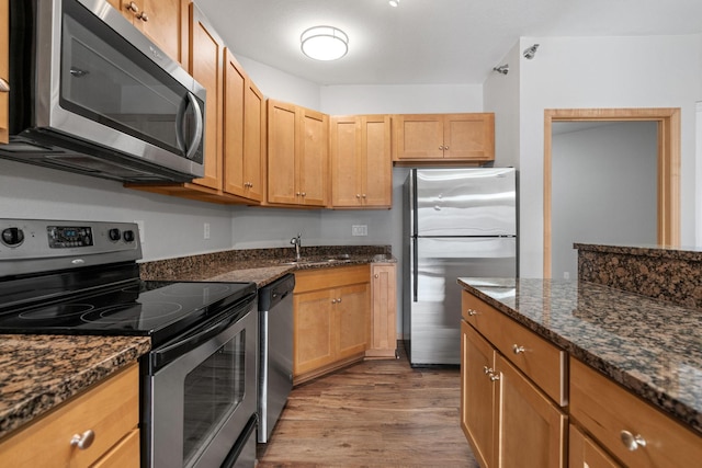 kitchen with stainless steel appliances, sink, wood-type flooring, and dark stone countertops