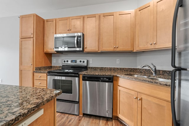 kitchen with appliances with stainless steel finishes, sink, light hardwood / wood-style flooring, and dark stone countertops