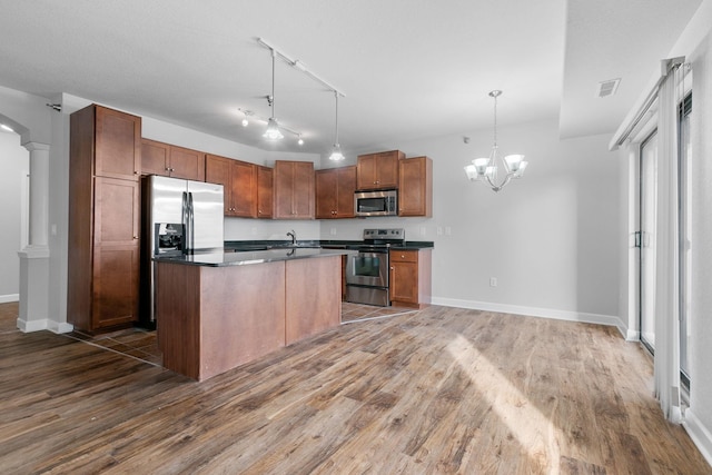 kitchen featuring dark hardwood / wood-style floors, stainless steel appliances, decorative light fixtures, and a center island with sink