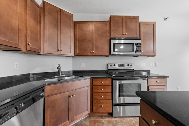 kitchen with dark stone countertops, sink, stainless steel appliances, and a textured ceiling