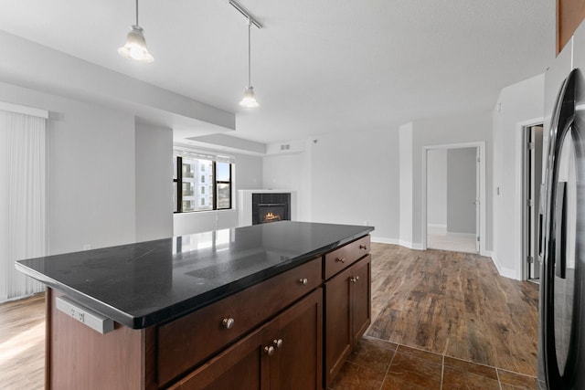 kitchen featuring stainless steel fridge, dark hardwood / wood-style floors, a fireplace, a kitchen island, and decorative light fixtures