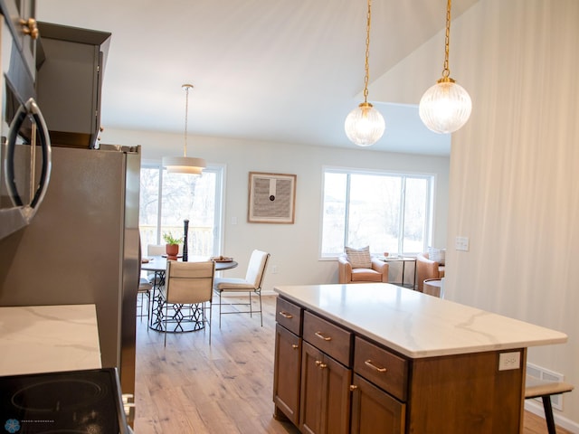 kitchen featuring pendant lighting, light hardwood / wood-style floors, light stone countertops, and appliances with stainless steel finishes