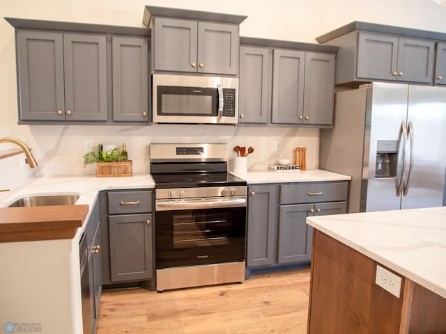 kitchen with light stone countertops, appliances with stainless steel finishes, gray cabinetry, sink, and light hardwood / wood-style floors