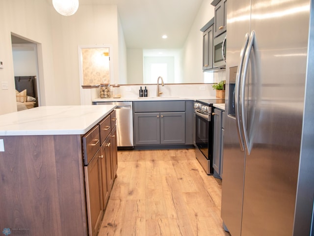 kitchen with gray cabinetry, light stone countertops, sink, light hardwood / wood-style floors, and appliances with stainless steel finishes