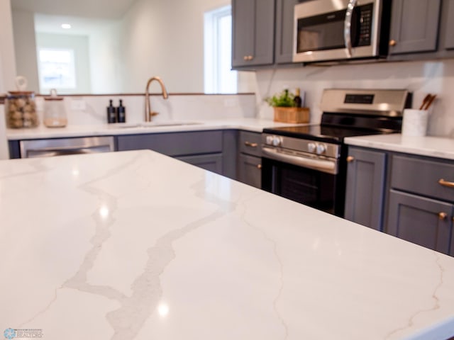 kitchen featuring light stone countertops, appliances with stainless steel finishes, gray cabinetry, and sink