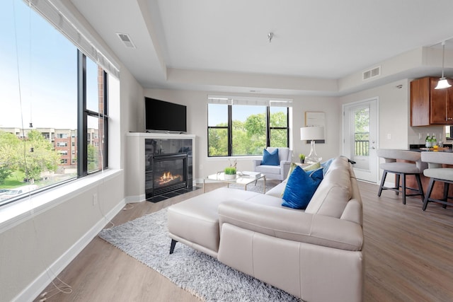 living room featuring a tray ceiling, a tile fireplace, and light hardwood / wood-style flooring