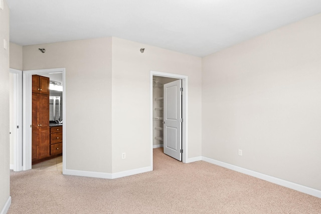 unfurnished bedroom with a walk in closet, light colored carpet, ensuite bath, and a closet