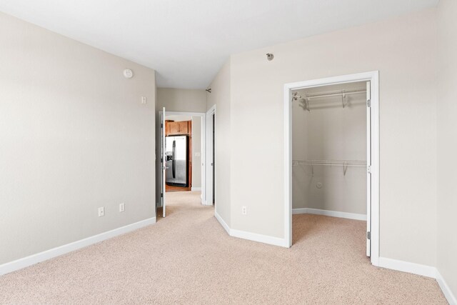 unfurnished bedroom featuring stainless steel refrigerator with ice dispenser, a closet, a spacious closet, and light carpet