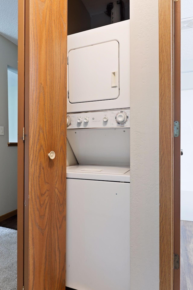 laundry room with carpet, stacked washing maching and dryer, and a textured ceiling