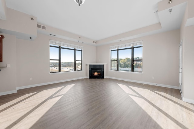 unfurnished living room with a raised ceiling, a tile fireplace, and light wood-type flooring