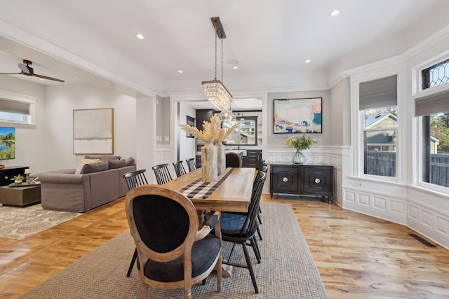 dining area featuring ceiling fan with notable chandelier, light wood-type flooring, and crown molding