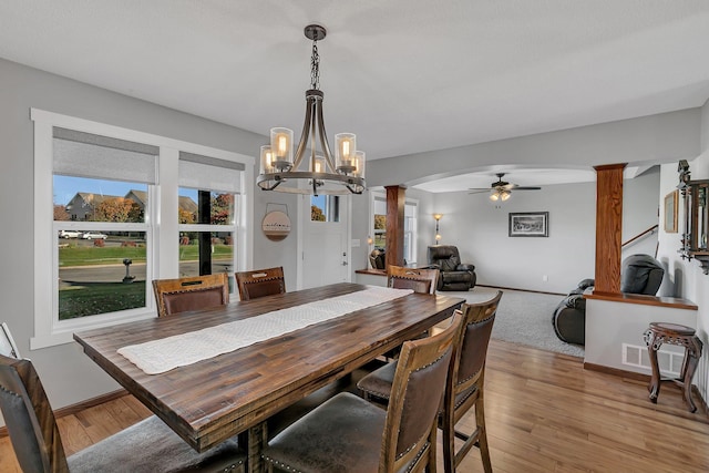 dining room with ceiling fan with notable chandelier, decorative columns, and light hardwood / wood-style floors