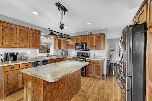 kitchen with a center island, black appliances, sink, hanging light fixtures, and light hardwood / wood-style flooring