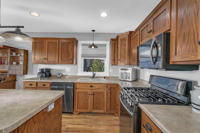 kitchen with pendant lighting, sink, stainless steel appliances, a textured ceiling, and light hardwood / wood-style flooring