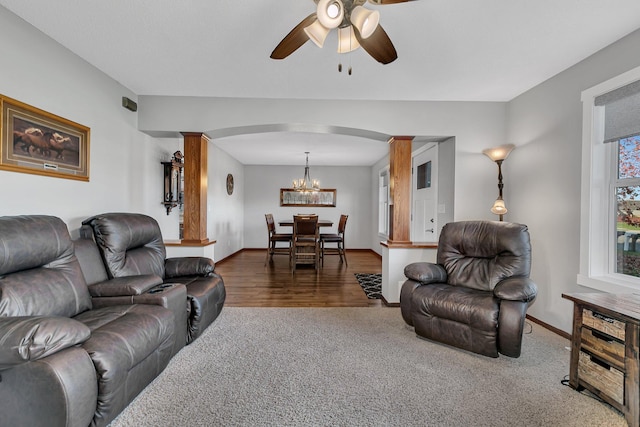 carpeted living room with ceiling fan with notable chandelier and decorative columns