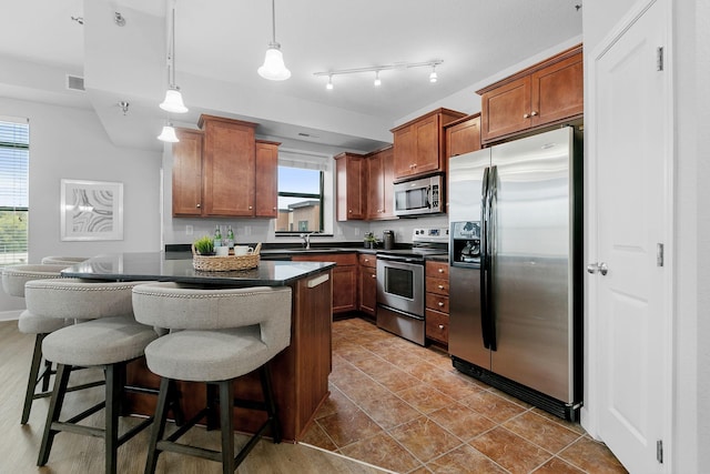 kitchen featuring light tile patterned floors, sink, hanging light fixtures, stainless steel appliances, and a kitchen bar