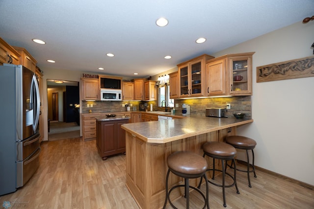 kitchen featuring a kitchen bar, sink, light hardwood / wood-style flooring, stainless steel fridge, and kitchen peninsula