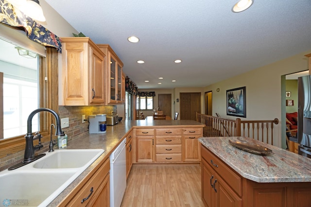 kitchen featuring sink, light hardwood / wood-style flooring, white dishwasher, kitchen peninsula, and backsplash