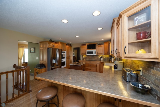 kitchen with hardwood / wood-style floors, tasteful backsplash, a kitchen bar, kitchen peninsula, and stainless steel appliances