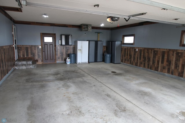 garage featuring a garage door opener, white refrigerator with ice dispenser, and wooden walls