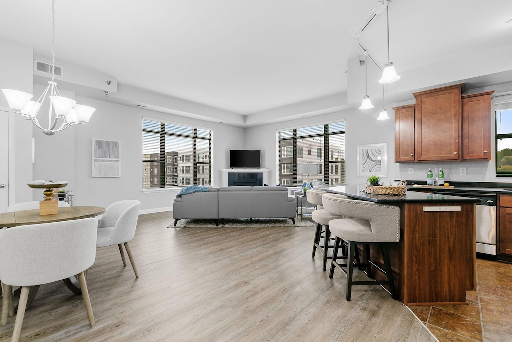 kitchen with a wealth of natural light, a kitchen bar, hanging light fixtures, a center island, and stainless steel dishwasher